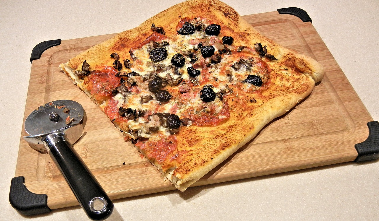 Immagine di una pizza fatta in casa con una consistenza gommosa su un tagliere di legno.