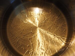 Immagine di un soffritto in padella, con olio e verdure, mentre si aggiunge un cucchiaio d'acqua.