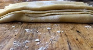 Pasta fresca stesa perfettamente su un piano di lavoro, con un mattarello e farina sparsa.