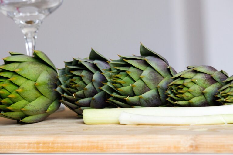 Carciofi freschi su un tavolo con limone e guanti per la pulizia senza annerire le mani.