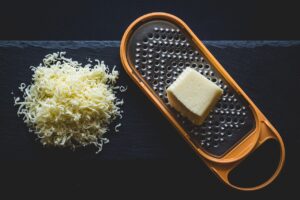 Formaggio molle grattugiato con il trucco del freezer, su un tagliere di legno.